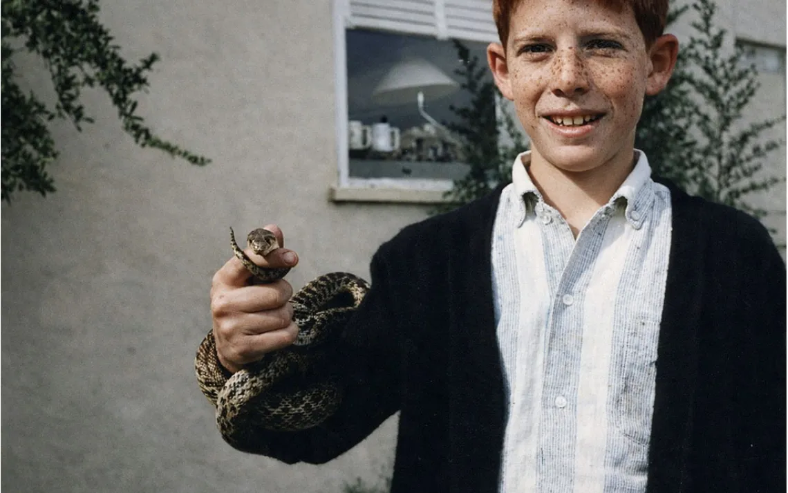 A young, freckled Bill Toone holds a gopher snake out toward the camera.