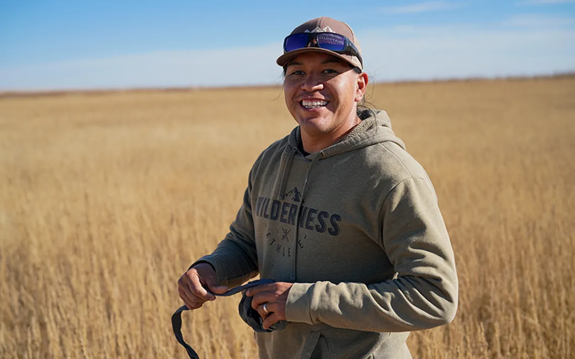 Lance Bernal stands in a dry-grass meadow and smiles at the camera
