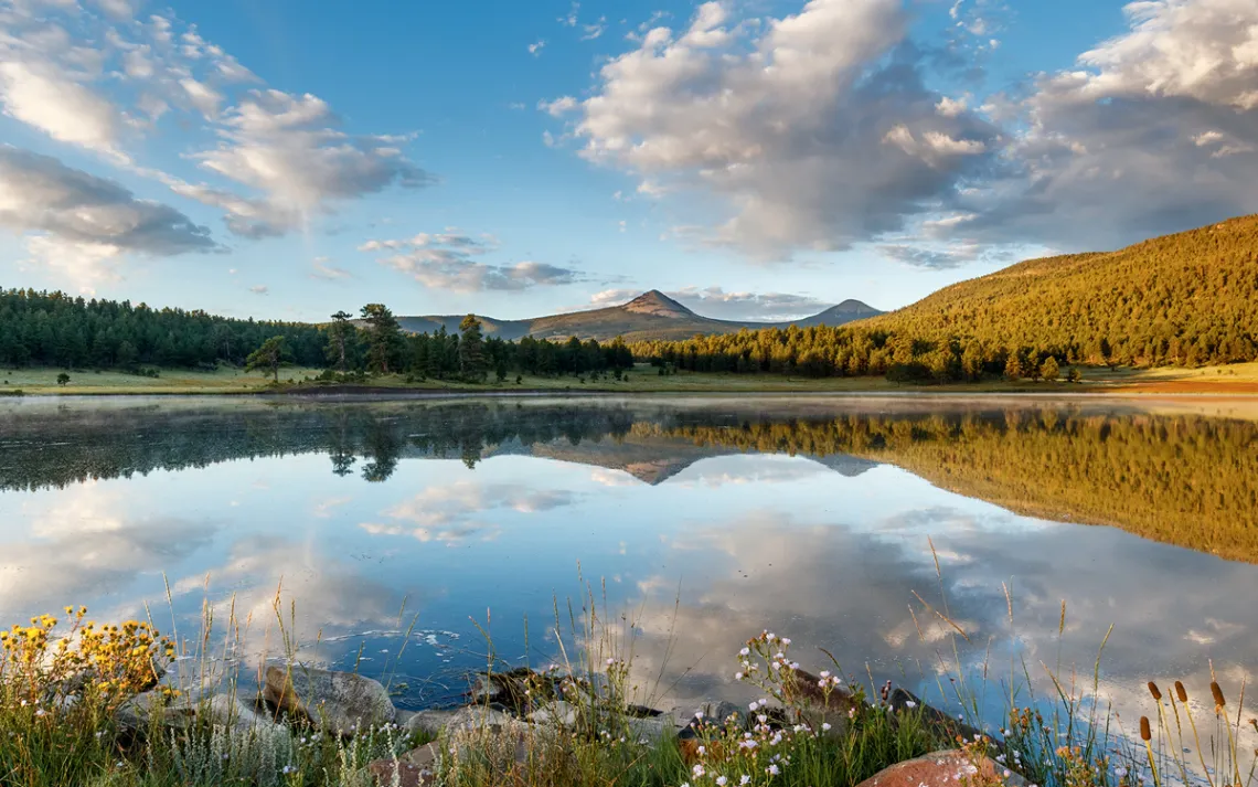 Calm-looking Munn Lake with the blue sky, mountains, and trees reflected off its surface