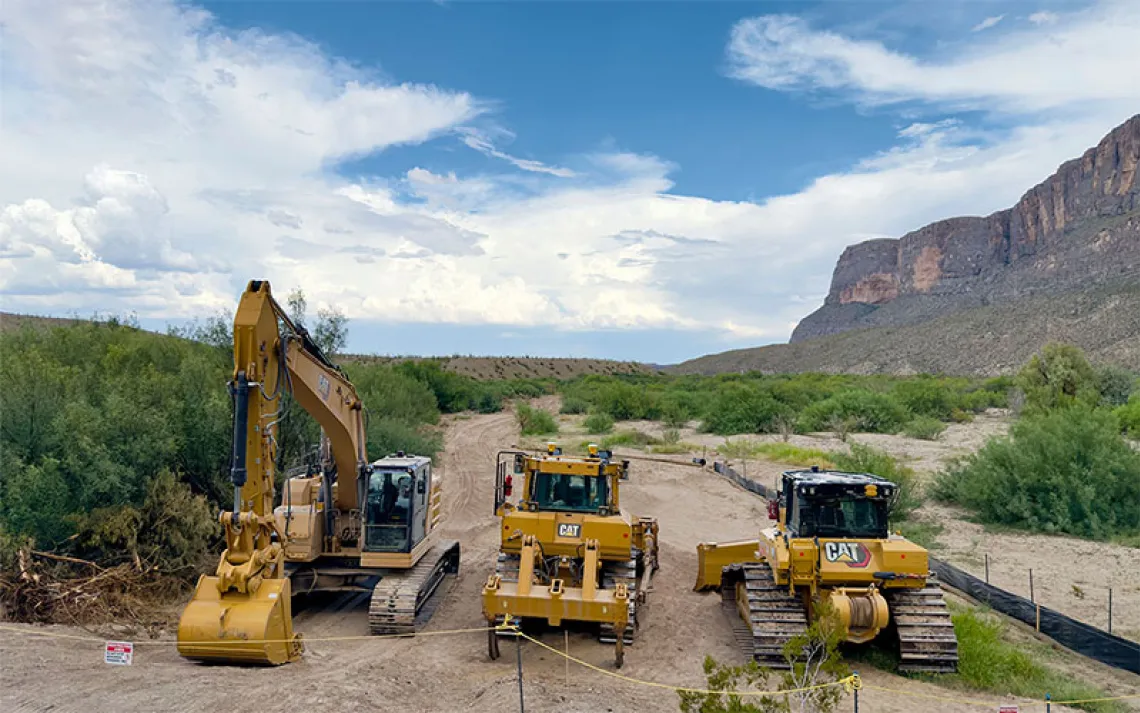 Construction trucks stand idyl along a section of the yet-to-build border wall.