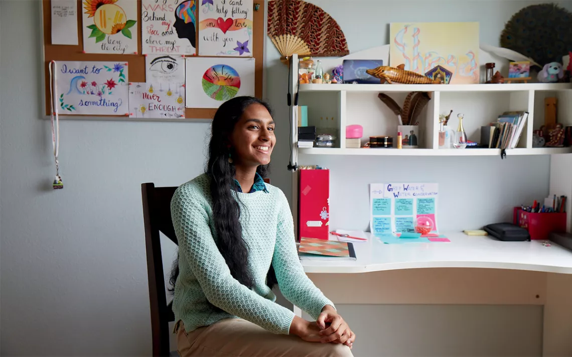 Shreya Ramachandran sits in a chair in her room smiling