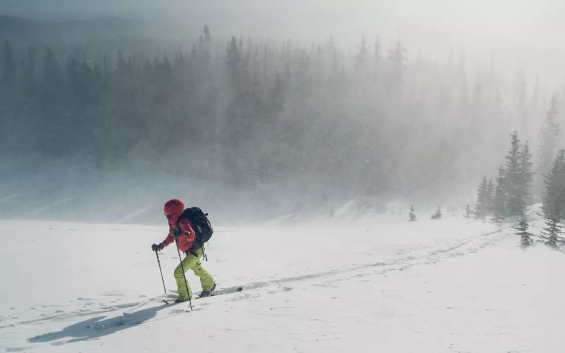 A backcountry skier slides uphill in the snow through a heavy mist.