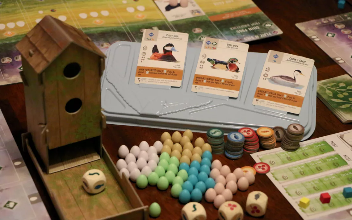 The components of the game Wingspan, including a small birdhouse, eggs, bird cards, food chips, and customized dice.