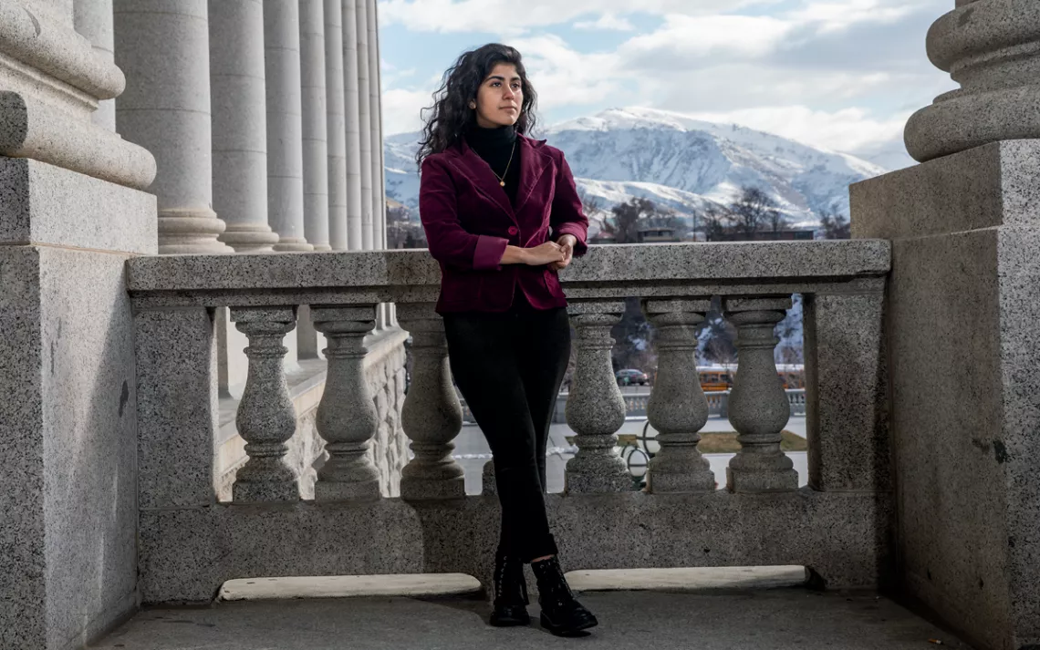 Mishka Banuri stands on a stone balcony with snowy mountains in the background, in Utah