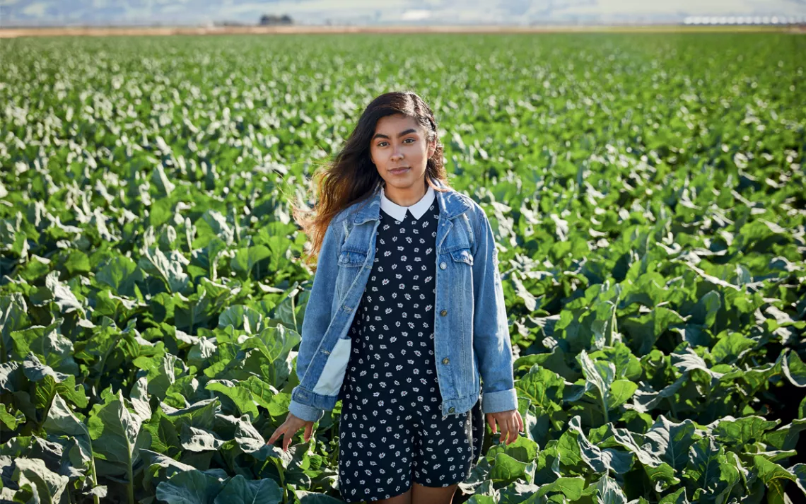 Magaly Santos stands in front of what appears to be a field of lettuce.