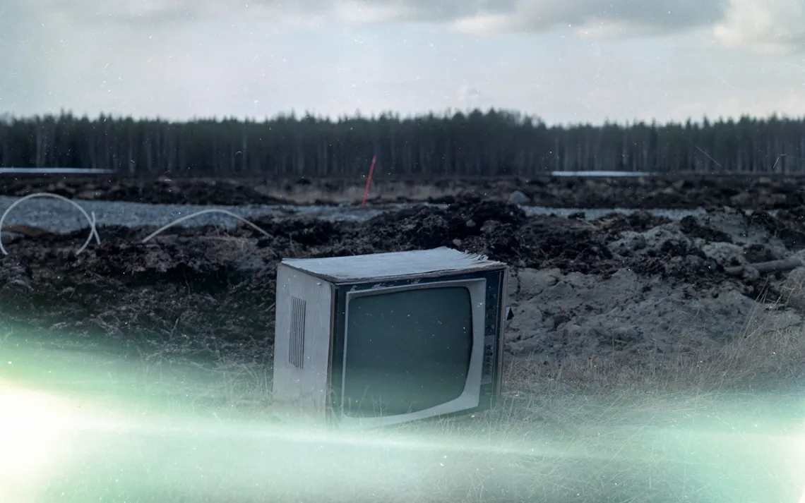 An old TV sits on the ground with a forest in the background.