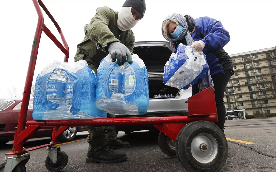 People in face masks loading bottles of water from a car and on to a red hand truck