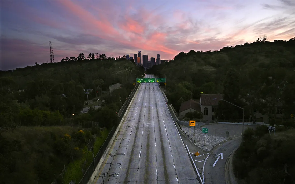 An empty highway surrounded by greenery seen from the air, reaching into a pink purple sunset.