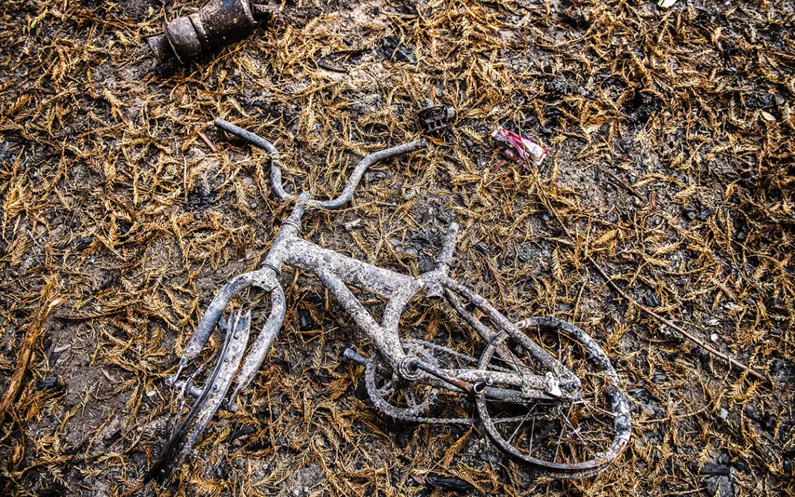 Scorched and soot-covered white bicycle lying on the leaf-covered ground. 