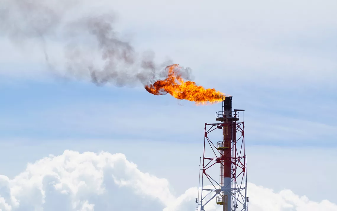 A bright orange flame nand smoke coming out of an oil well against a light blue sky