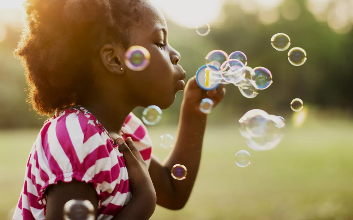 Black girl blowing bubbles in a green and verdant landscape