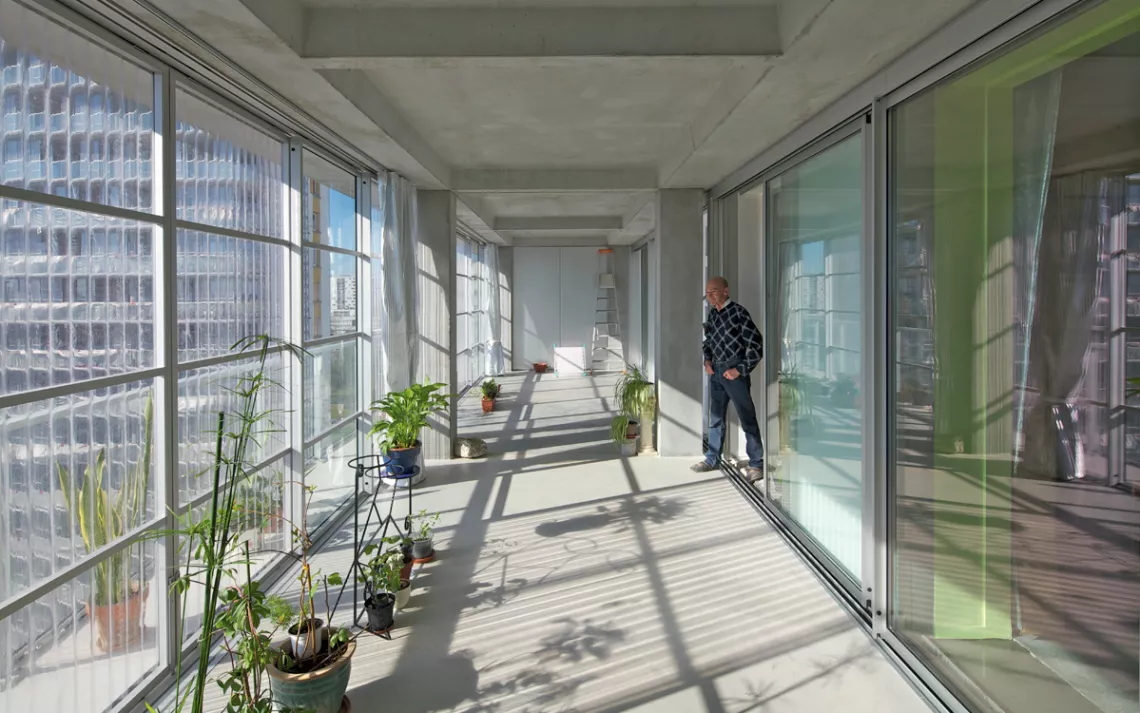A man walks out of a unit onto a sun-lit balcony with potted plants.