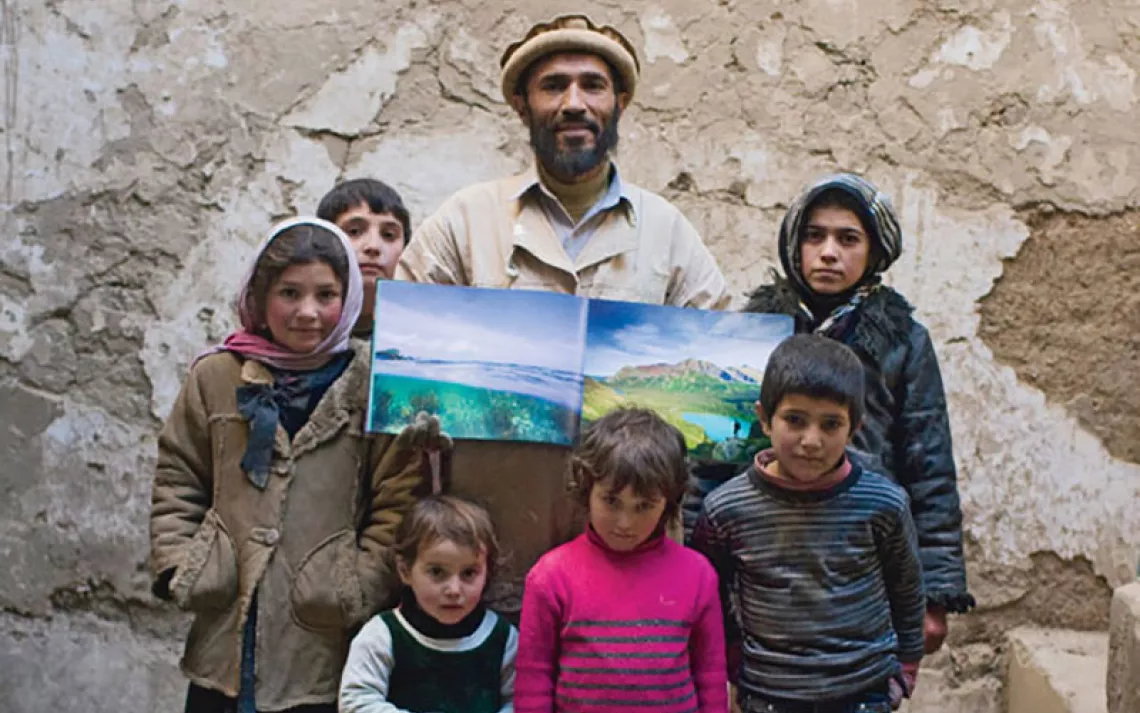 Outside a house he's building for his family and surrounded by his children, Muhammad Jan, a 46-year-old builder and plasterer, displays photos of Biscayne National Park in Florida and Glacier National Park.