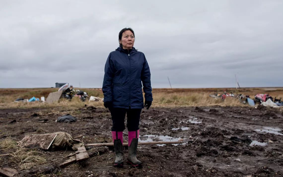 Charlene Carl, in waders, stands on muddy ground where her home used to be in Newtok, Alaska.