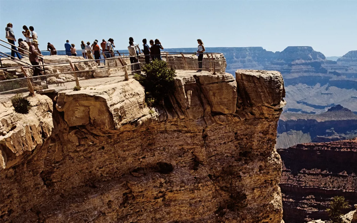 Close-up of a ledge in the Grand Canyon. People are looking over the edge and taking photos.
