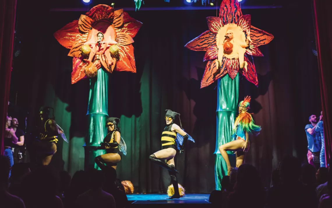 Nate and Hila perform "Plant Sex" at the House of Yes in New York. They are each sitting in a huge flower while people in insect costumes dance below.