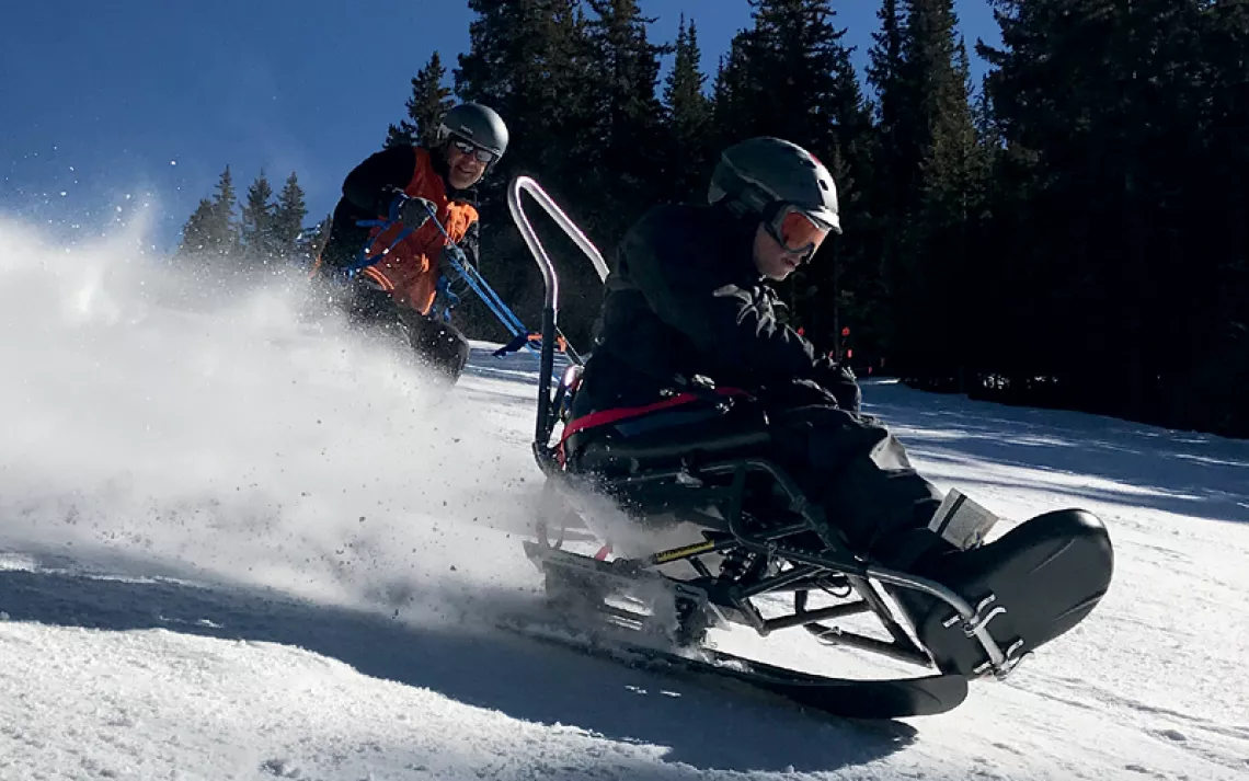 Two people are flying down a ski slope with an Enabling Technologies Dynamique Bi Ski.