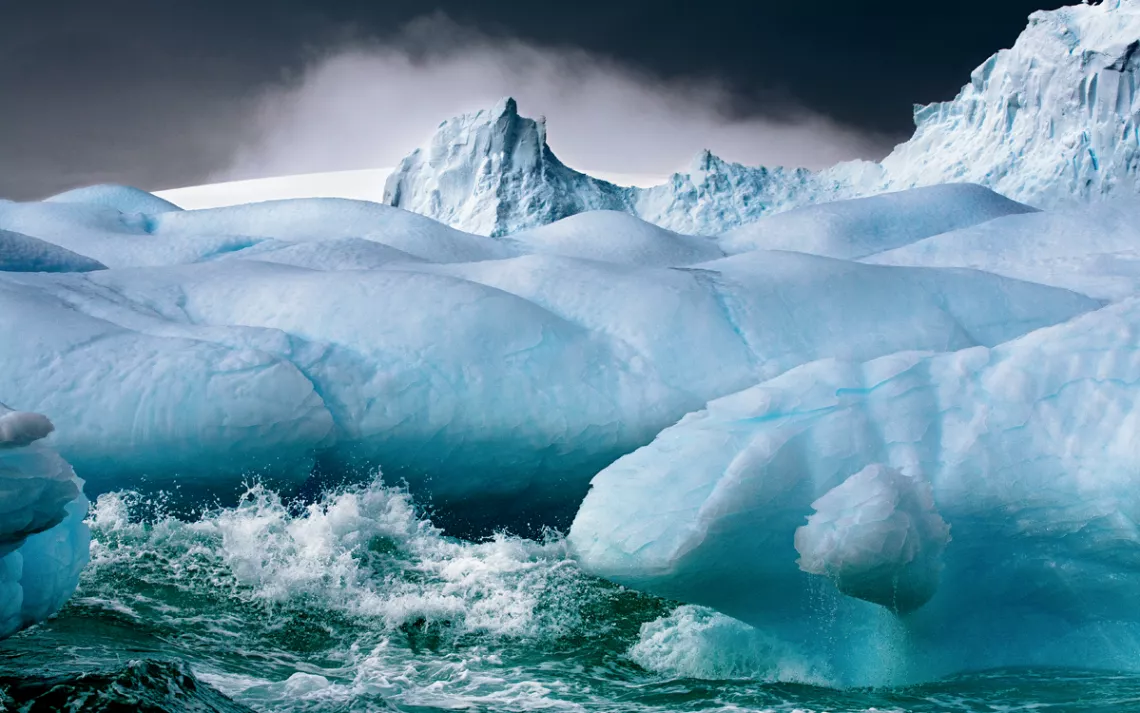 Waves splash against a blue iceberg in Antarctica