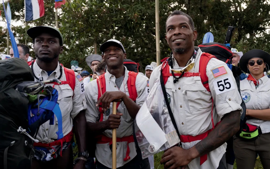 Several members of Team Onyx wear off-white shirts and red backpacks. One is holding a plastic bag with a compass and other items.