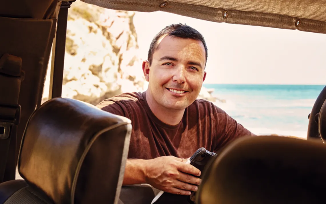 Brian Holguin looks into a car (or cart) and smiles at the camera inside.
