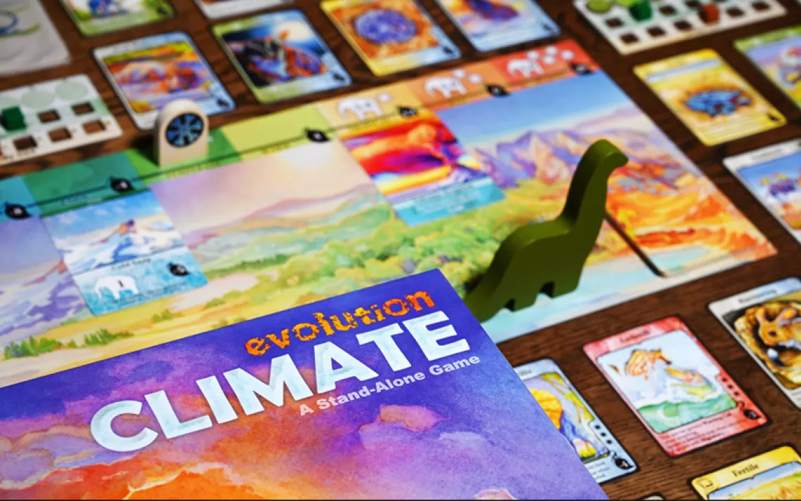 Box for tabletop game "Evolution" with colorful cards and game pieces arrayed around it.