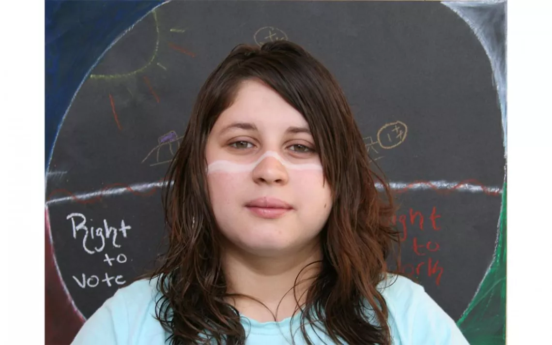 A student artist who attended Ajo High School in Ajo, Arizona. Each student was asked to create a symbol representing their experience on the border, draft that symbol in clay sculpture, and draw it on paper to form the background of their portrait. | Pho