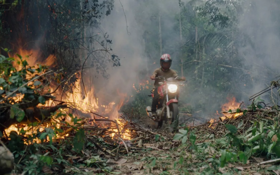A person in a small dirtbike rides through a rainforest that is on fire.
