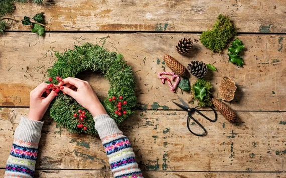 Overhead view of an arrangement of a Christmas wreath or garland being made by a teenage girl. Various tools and decorative pieces are laid out waiting to be used. 