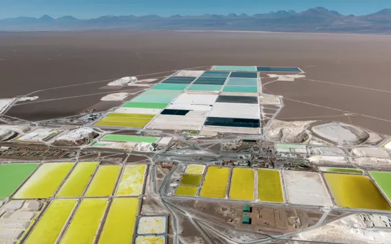 Aerial photo of a dark-sand desert with several shallow lithium pools in greens and blues and yellows.