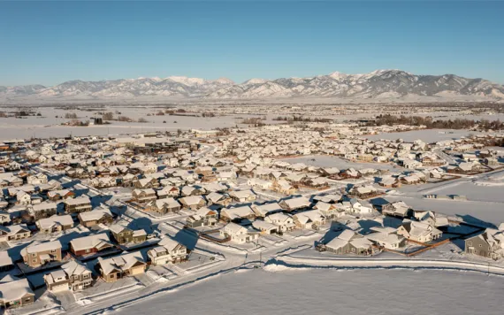 Aerial photo shows a flat housing subdivision covered in snow with mountains in the background.