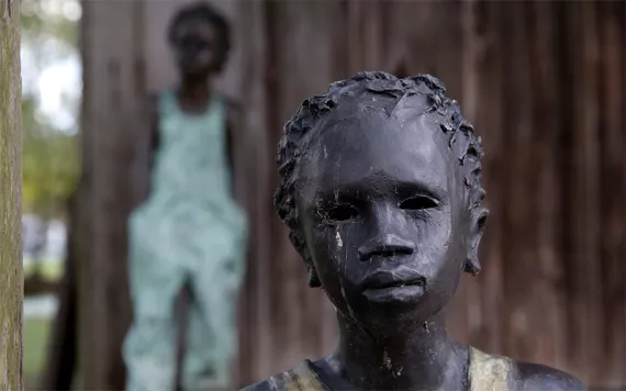 This July 14, 2017 photo shows two of the 40 statues spread throughout the grounds, titled "Children of Whitney" by Woodrow Nash, in front of one of the slave cabins at the Whitney Plantation in Edgard, La.