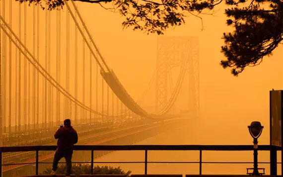 A man talks on his phone as he looks through the haze at the George Washington Bridge from Fort Lee, N.J., Wednesday, June 7, 2023.