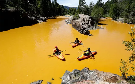 People kayak in water colored from a mine waste spill at the Animas River near Durango, CO