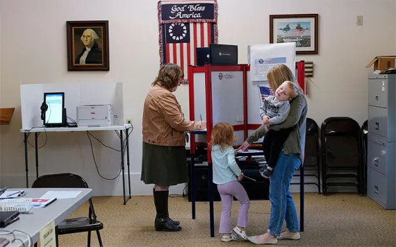 Lauren Miracle, right, holds her son Dawson, 1, as she helps her daughter Oaklynn, 3, fill out a child's practice ballot before voting herself at a polling location in the Washington Township House in Oregonia, Ohio, Tuesday, Nov. 7.