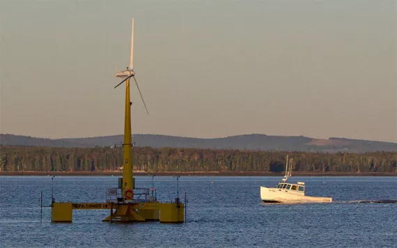 Offshore wind turbine floats off the coast of Maine with a lobster boat and forest in the background