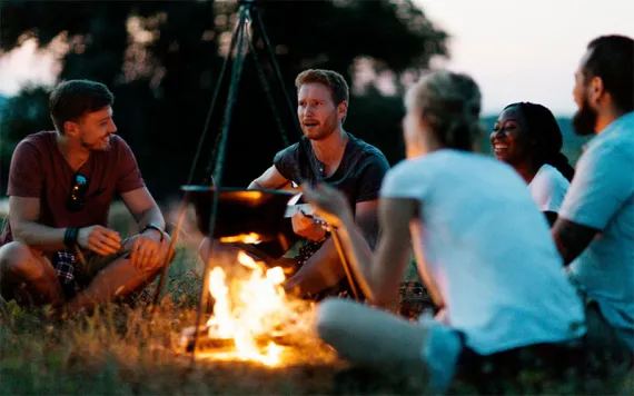 People sitting in a meadow around a campfire at dusk