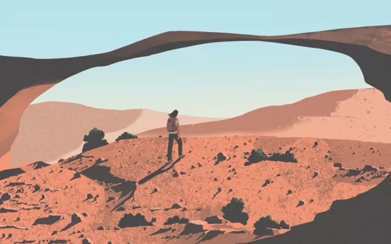  A hiker walks up a redrock hill toward a sandstone arch in the desert