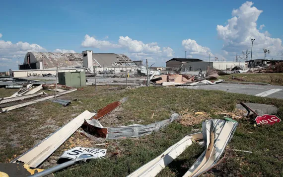 Tyndall Air Force Base is littered with debris after Hurricane Michael. A hangar's roof is missing tiles. Metal pieces, including a Stop sign, are on the ground.