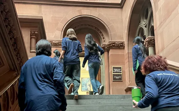 Students and adults from CRETF wearing black pants and dark-blue tops walk up the steps of the New York State Capitol.