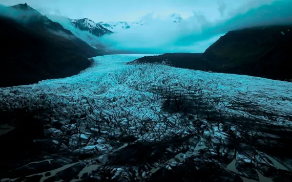 A dark sky and mist appear above the mountain and ice of Svínafellsjökull glacier in Iceland.
