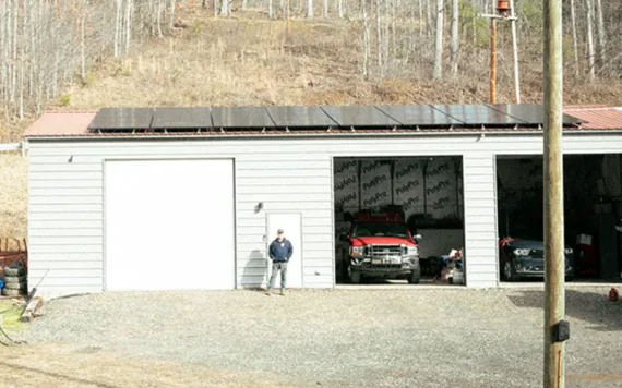 A man stands before a fire department building with solar panels affixed to the roof. 