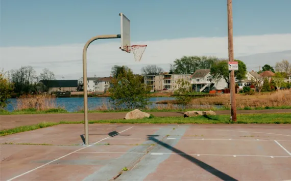  A basketball court at water level with houses lined along the shore.