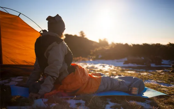 A girl looking toward the sun from her tent while snuggled in her sleeping bag