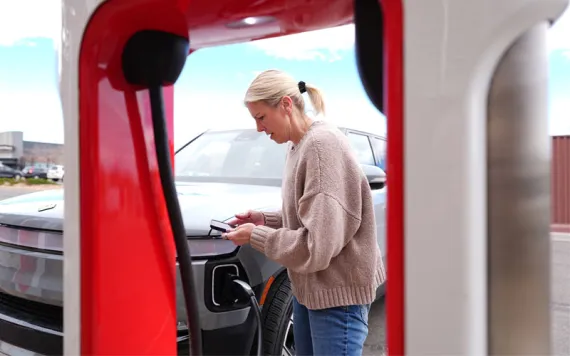 A driver, seen through an EV charging station, powering her EV SUV.