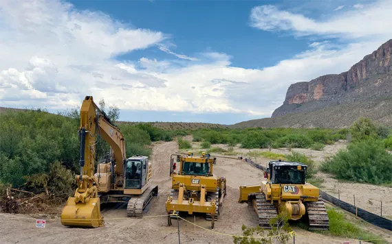 Construction trucks stand idyl along a section of the yet-to-build border wall.