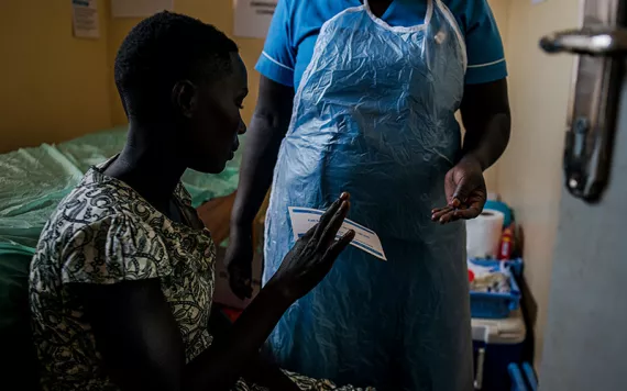 A woman in Uganda wearing a printed dress is handing a nurse a paper.