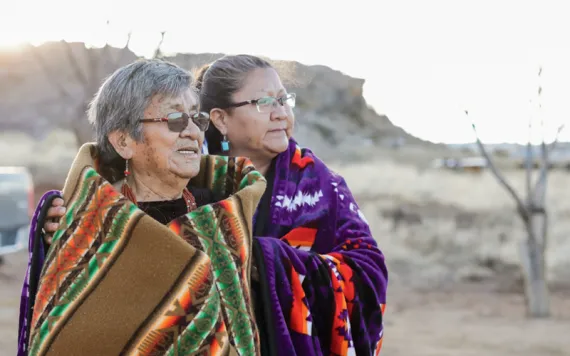 Jessie and Verma Harrison stand together, both wearing blankets around their shoulders and looking off in the distance.