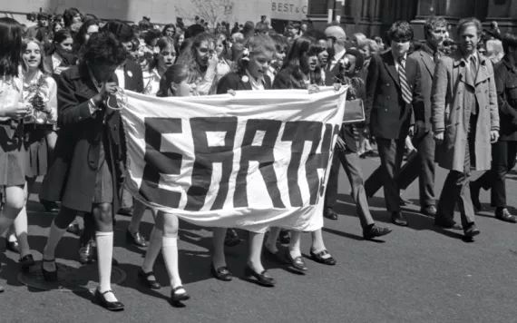 Students in their school uniforms walk and hold a banner that says Earth, on the first Earth Day in 1970.