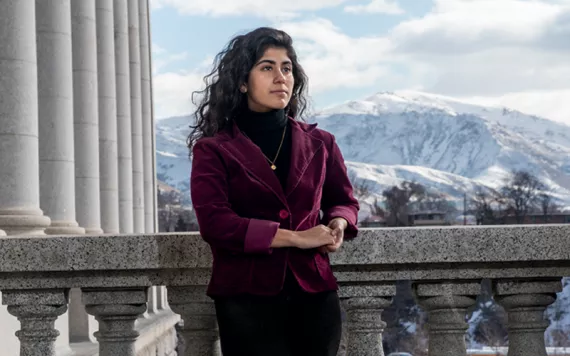 Mishka Banuri stands on a stone balcony with snowy mountains in the background, in Utah