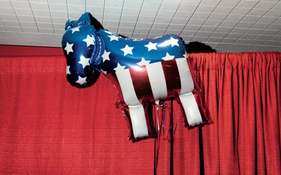A helium donkey balloon with stars and stripes hangs next to a red curtain